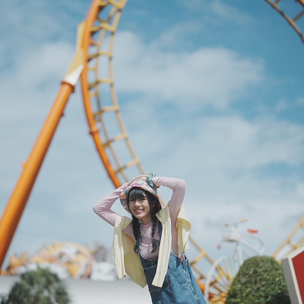 Excited girl with arms raised and hands on hat in front of a roller coaster