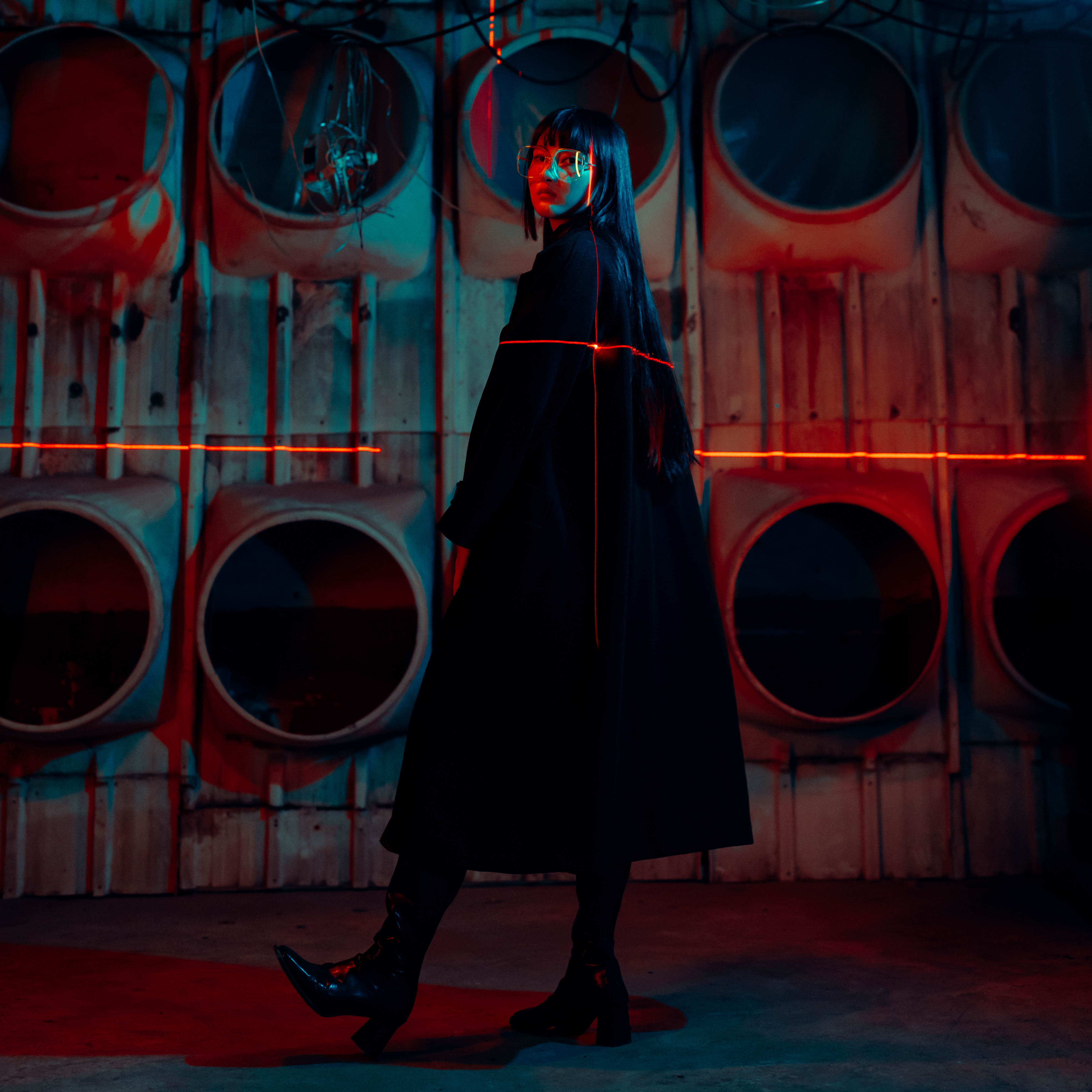 Side view of girl dressed in black in an abandoned warehouse, with a laser pointing across her body