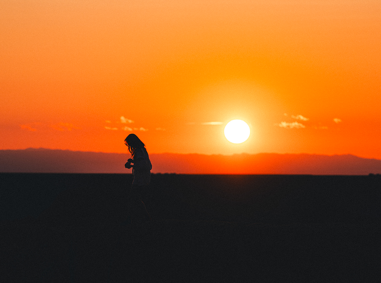 Silhouette of female holding a camera and walking with the setting sun in the background